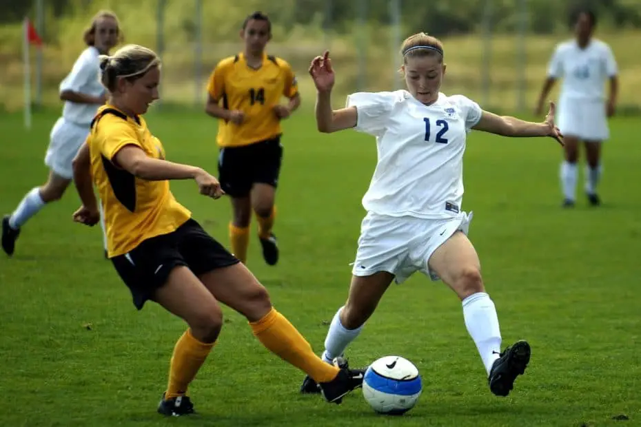 Women playing soccer, one team wearing white, the other yellow and black