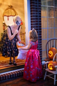 Girl trick-or-treating in a pink dress, woman with candy bowl