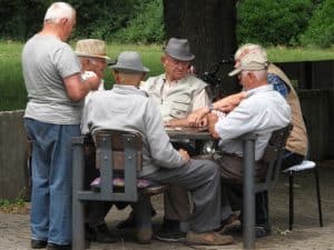 A group of 6 senior men playing cards at an outdoor table