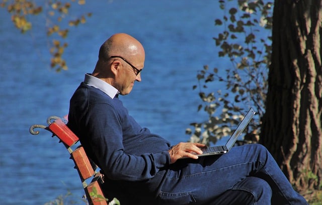 Senior man sitting by the lake with a laptop