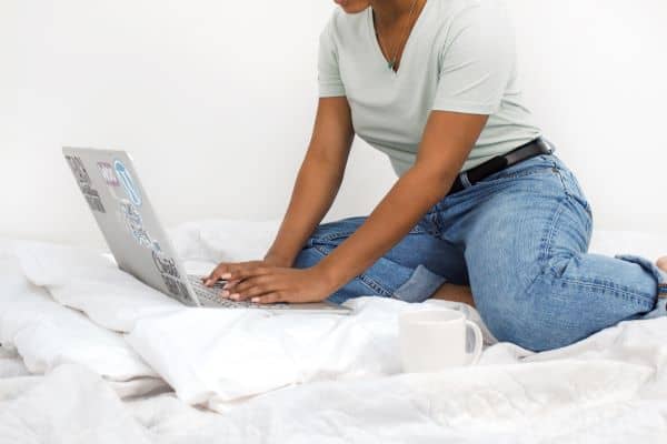 Woman sitting on bed typing on laptop