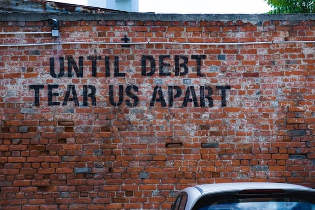 Until debt tear us apart painted on brick wall